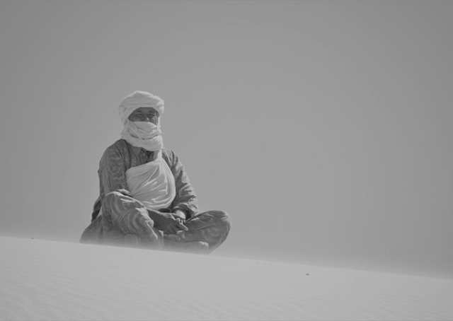 Un homme assis sur une dune dans un désert en Algérie